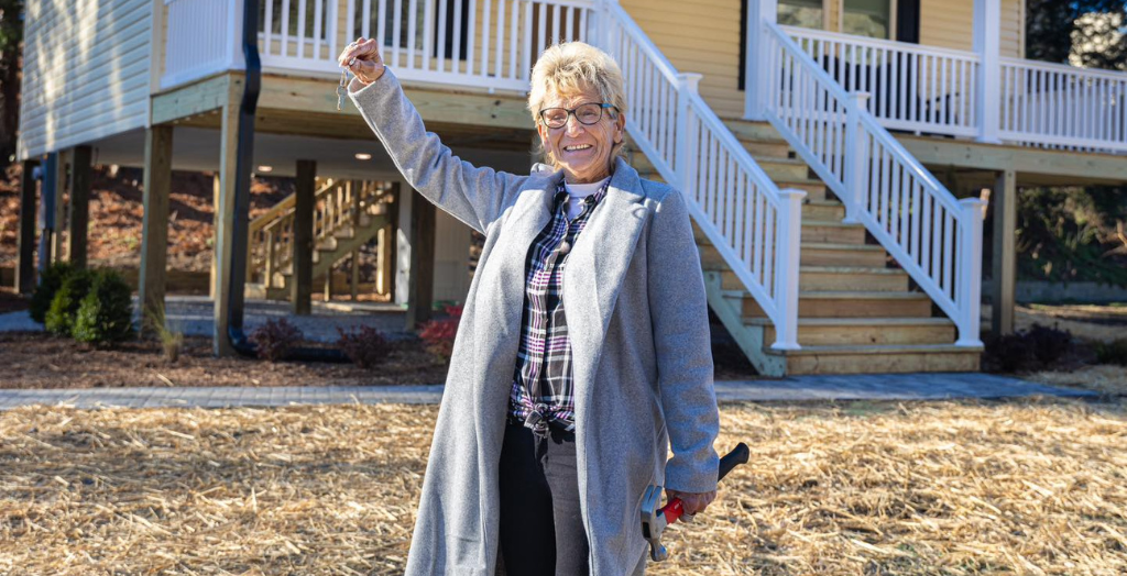 Person in a gray coat raising their fist outdoors near a house.