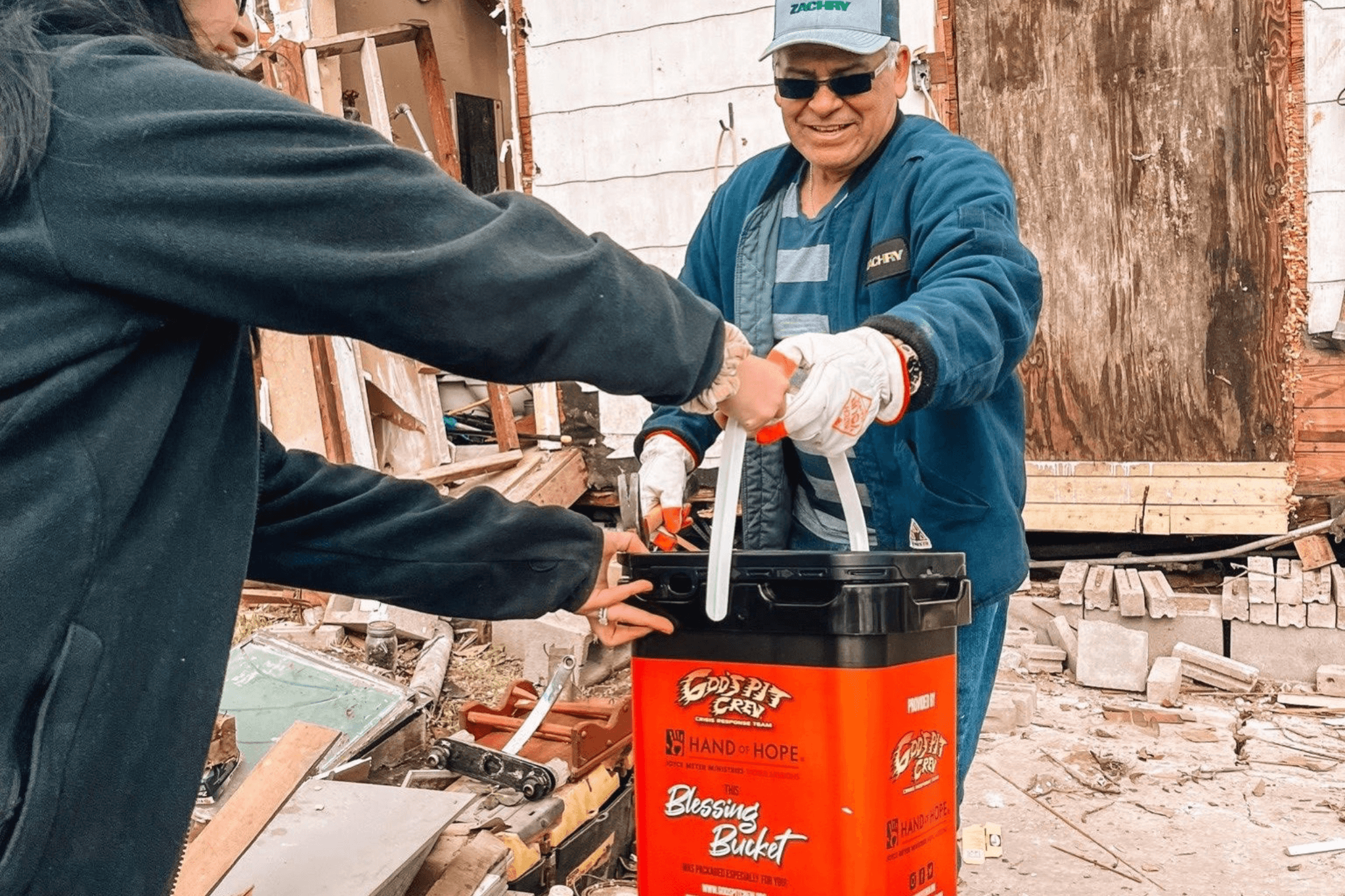Two people passing a bucket with tools on a construction site.