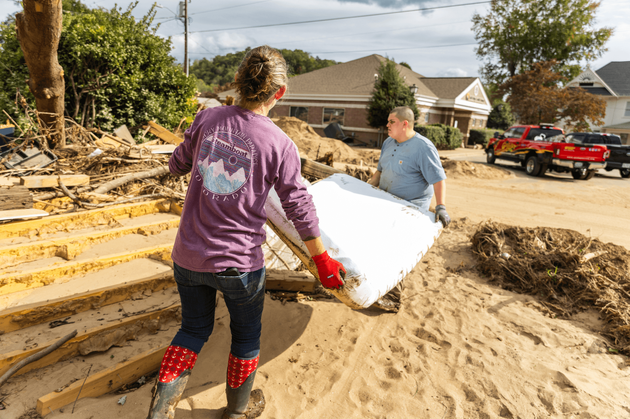Two people carrying a large white object outdoors in a sandy area.