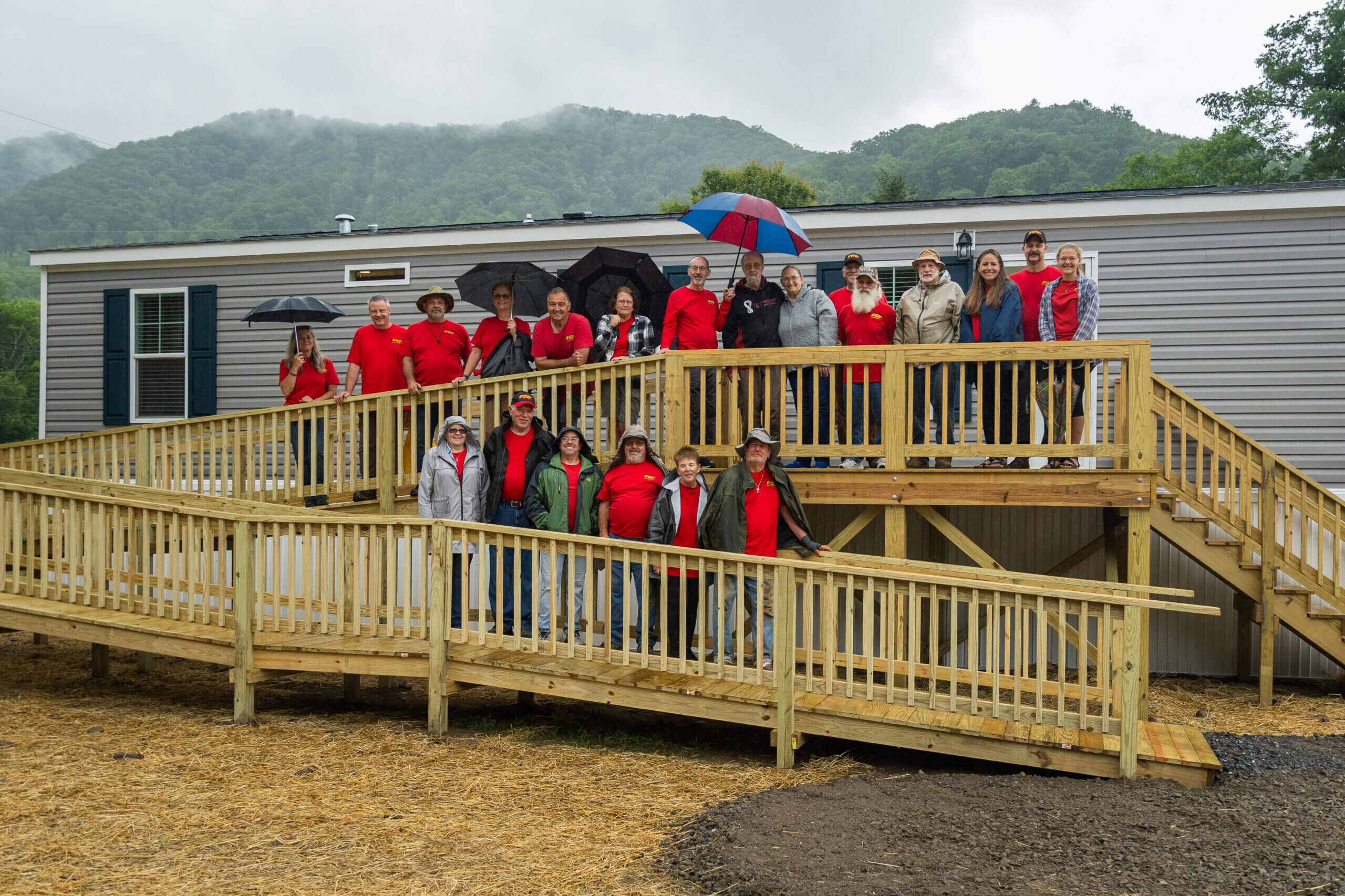 Group of people in red jackets standing on wooden walkways in a foggy outdoor setting.