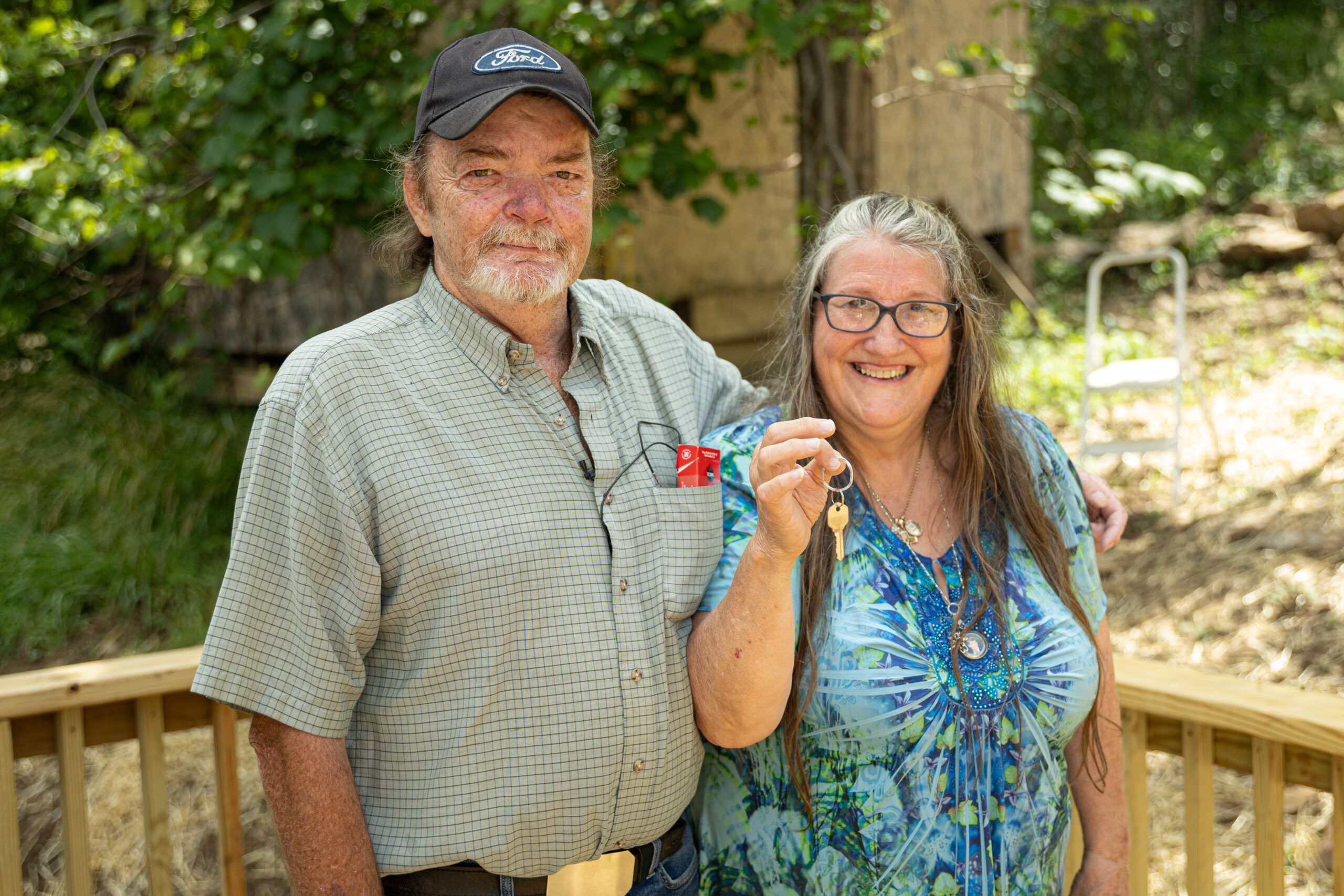 Smiling couple holding a small red object outdoors.