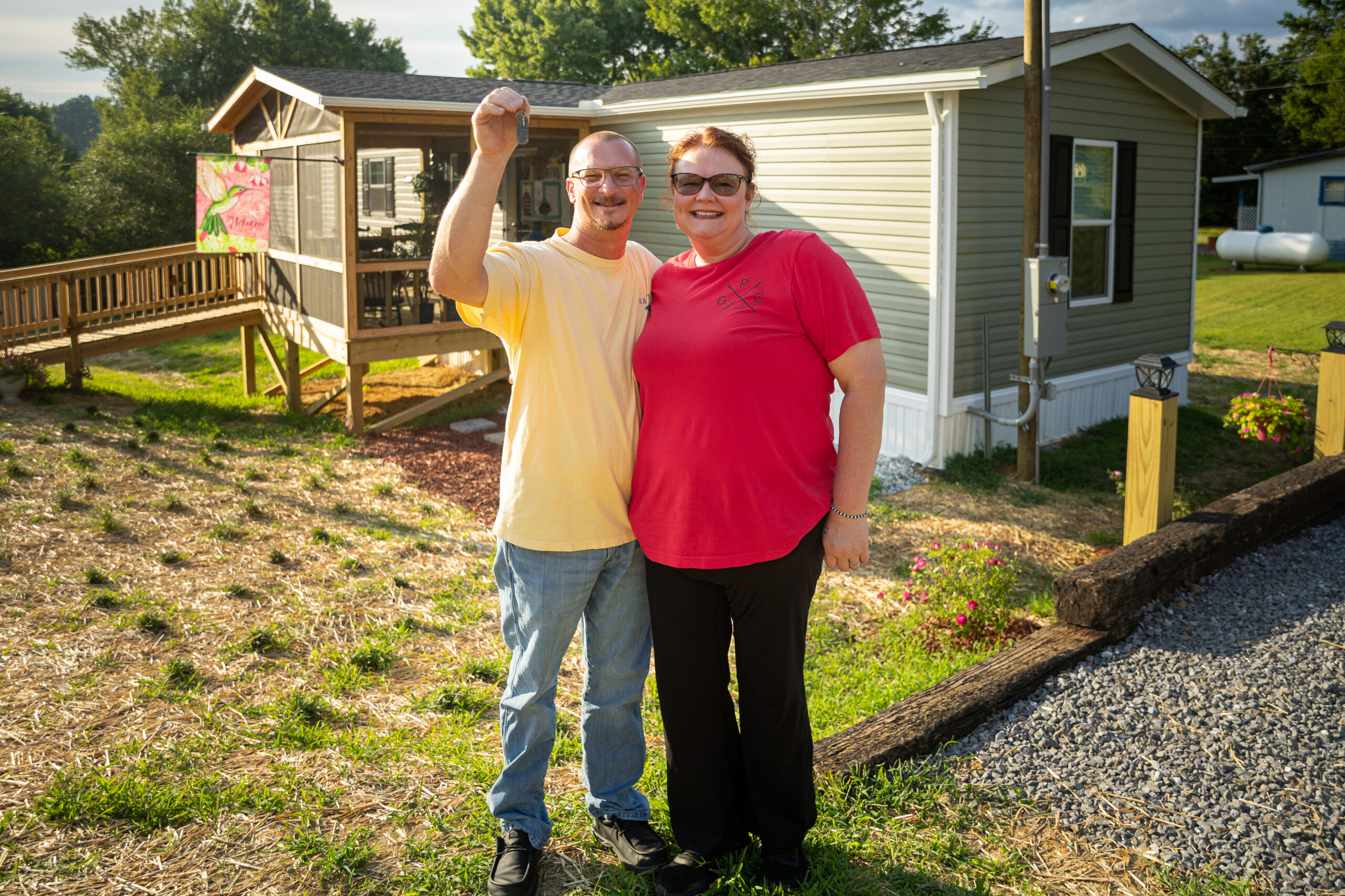 A smiling couple standing outside near a mobile home on a sunny day.